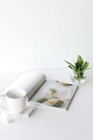 Coffee cup and book on white table with green plant.