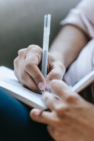 Close up of a man writing in a notebook while sitting on a sofa at homeの写真素材