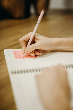 Close-up of a woman writing in a notebook. The girl is sitting at the table and writing something.の写真素材