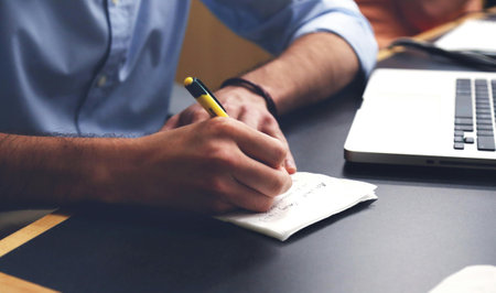 Close-up of man writing in notepad at desk in office