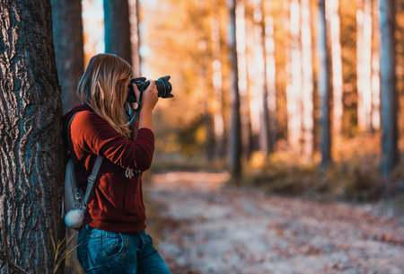 Young woman photographer with camera taking photo in autumn forest. Back viewの写真素材