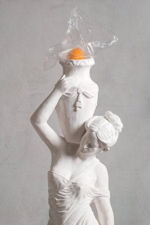 Statue of a woman with a towel on her head and an orange eggの写真素材