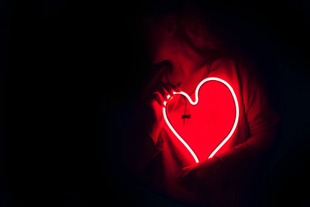 Red heart in the hands of a man in a dark room.の写真素材