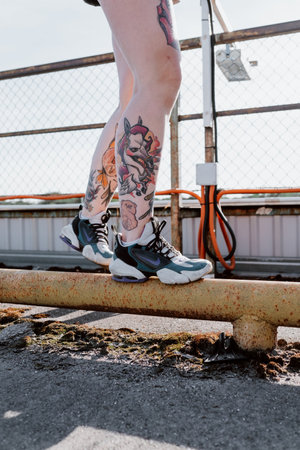 Tattooed female legs in sneakers on the background of a fence