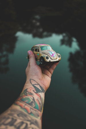 Tattooed hand holding a small toy car on a lake backgroundの写真素材