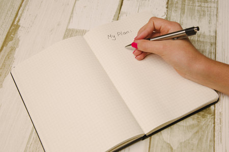 Woman's hand writing in notebook on wooden background. Top view.