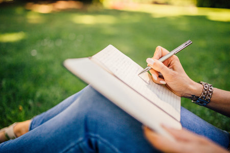Close-up of female hands writing in notebook while sitting on grass in parkの写真素材