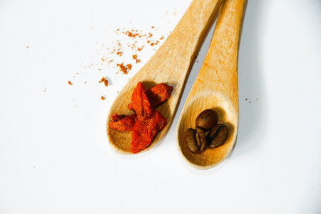 Coffee beans and dried tomatoes in wooden spoon on white backgroundの写真素材