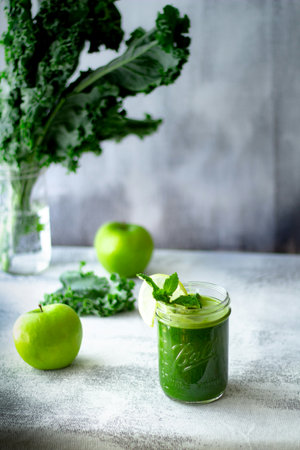 Green smoothie with kale, spinach, apple and mint in a glass on a light backgroundの写真素材