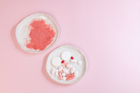 Top view of colorful pills and capsules on white plates over pink backgroundの写真素材