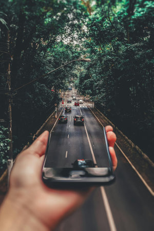 A man's hand is holding a smartphone with a view of the road through the trees.