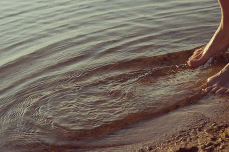 woman's feet making waves in the water on the seashoreの写真素材