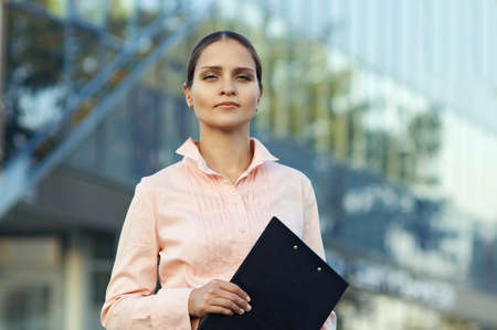 Business woman holding documents , standing against the office buildingの写真素材