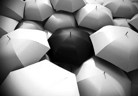 Black umbrella standing out from background of white umbrellasの写真素材
