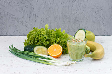 The concept of purification from detoxification, the ingredients of a green vegetable cocktail. Natural, organic healthy juice in a bottle for a diet for weight loss or fasting. Cucumber, apple, lemon and lettuce, banana, green onion isolated on white wood with copy space.の写真素材