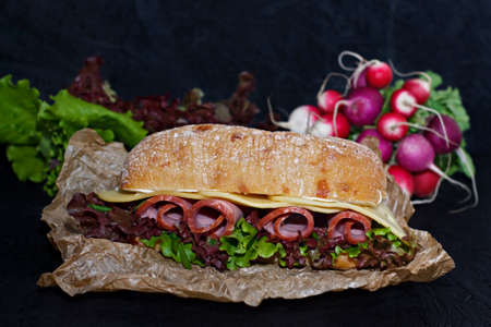 Sandwich of crispy ciabatta with ham, cheese and lettuce leaves on a dark background.