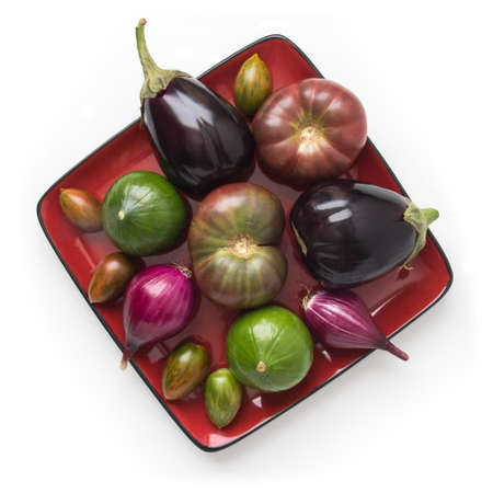 Organic tomatoes, squash, and onions on a square red plate, isolated on white, top viewの写真素材