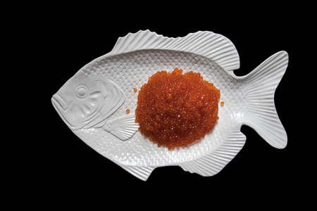 Red salmon caviar on a fish-shaped plate, isolated on black, top viewの写真素材
