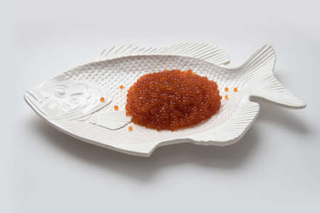 Red salmon caviar on a fish-shaped plate, isolated on whiteの写真素材