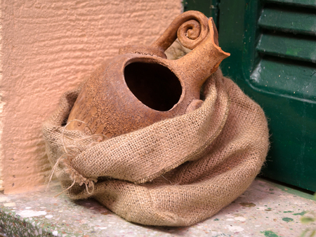 Clay jug in burlap on the windowsill. Vintage Design