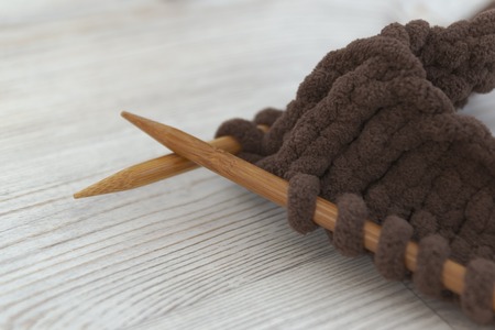 Wooden knitting needles and knitting from thick brown yarn. Close-up. Use as a demonstration of female craftsの写真素材