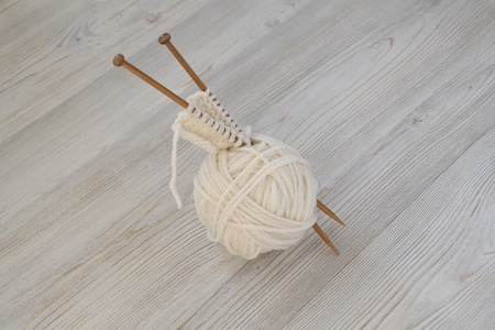 White ball of yarn and wooden knitting needles on the surface of wooden boards