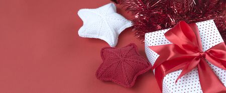 Christmas banner with gift box, tinsel, and knitted stars. Gift concept for needlewoman on a red background.の写真素材