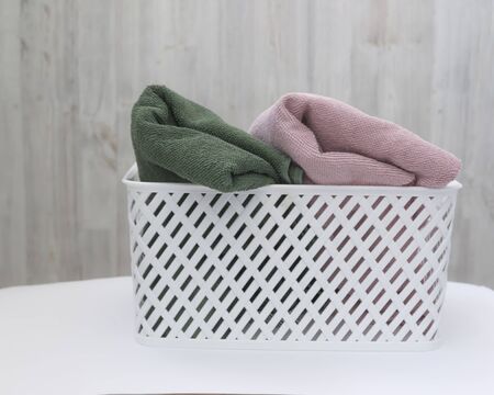 White plastic basket with clean multi-colored towels on a wall background