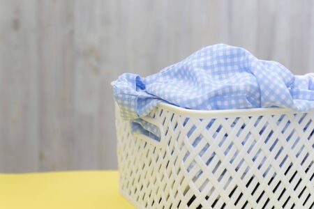 Blank blue white shirts in a white plastic basket on a yellow table on a gray background. Laundry, home cleaning, cleanliness and freshnessの写真素材