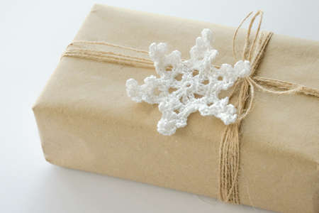 Christmas and New Year background. Gift box wrapped in kraft paper with jute cord. Decorated with a crocheted snowflakeの写真素材
