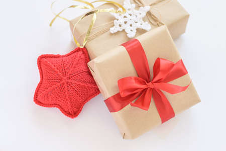 Christmas and New Years decorated gifts. Gift box wrapped in kraft paper with red ribbon. Red knitted heart. Box with jute cord and crocheted snowflakeの写真素材