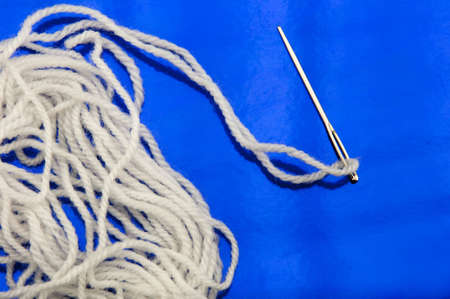 white thread and a sewing needle in a bright blue backgroundの写真素材