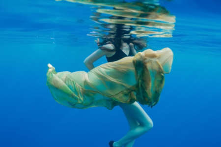 girl in a yellow skirt and its reflection on surface of the sea, underwater view.の写真素材