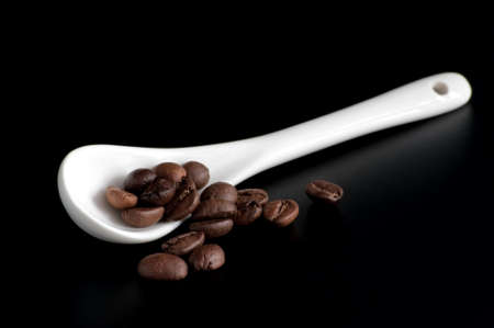 white spoon with coffee beans on a black  background の写真素材
