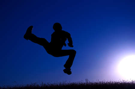 black silhouette of a jumping young man on a blue sky and sun backgroundの写真素材