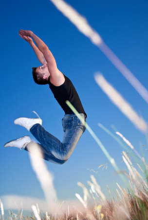 a young man jumping above the meadow against the blue skyの写真素材