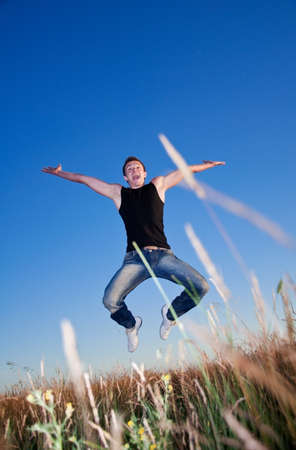 a young man hanging in the air above the meadow against the blue skyの写真素材