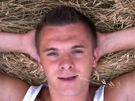 portrait of a young man with a straw in his mouth on a hay backgroundの写真素材