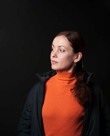 casual portrait of a brunette woman  in an orange sweater and dark  jacket on a black backgroundの写真素材
