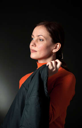 casual portrait of a brunette woman  in an orange sweater and dark  jacket on a black backgroundの写真素材