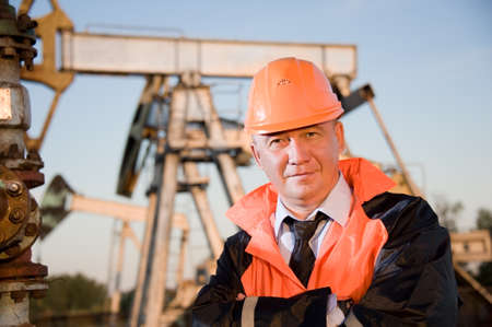 Oil worker in orange uniform and helmet on of background the pump jack and blue sky.の写真素材