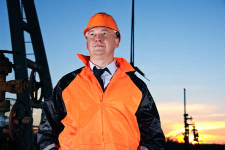 Oil worker in orange uniform and helmet on of background the valves, piping and sunset sky.の写真素材