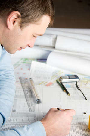 Architect or engineer in blue pullover is working on construction plans 