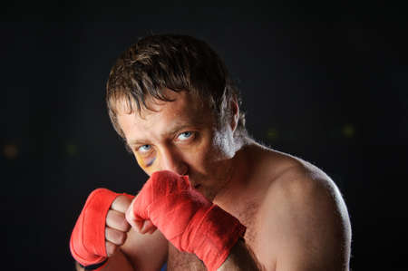 Portrait of a man with a bruise in a battle position  Clenched fists  Dark background 