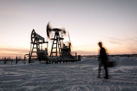 Oil worker in a oilfield. Pump jack and engineer on a winter sunset sky background. Western Siberia. Blurred motion.の写真素材