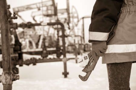 Working hand with wrenches on a wellhead crude oil site background. Toned sepia.の写真素材