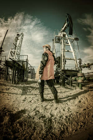 Women worker in the oil field, with wrenches in a hands, orange helmet and work clothes. Industrial site background. Toned.の写真素材