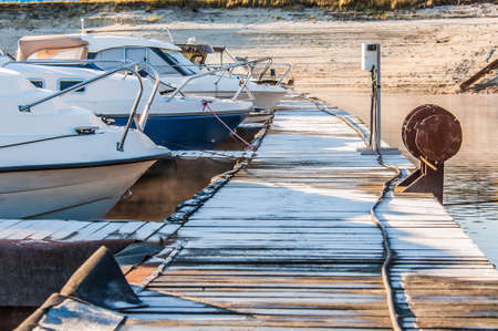 Boats and yachts moored at the port. Glittering sea surface against sunrise. Morning fog.の写真素材