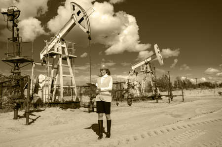 Woman engineer in glasses on the oil field wearing helmet and work clothes. Industrial site background. Oil and gas concept. Toned sepia.の写真素材