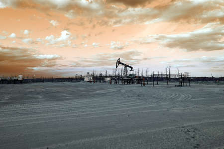 Oil pump jack and wellhead with valve armature during sunset on the oilfield. Extraction of oil. Oil and gas concept. Toned.の写真素材